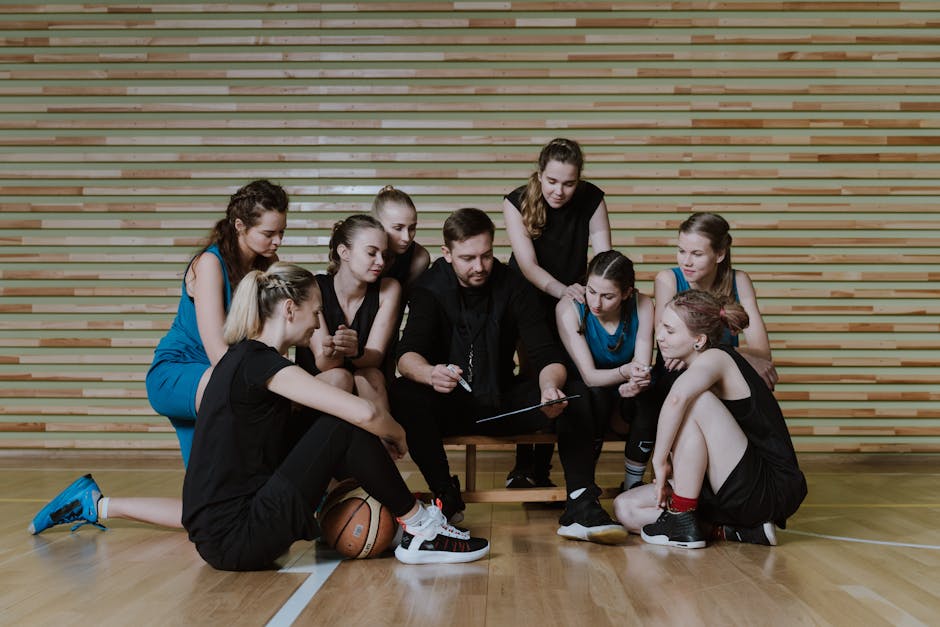 A coach strategizes with a women's basketball team in a gymnasium.